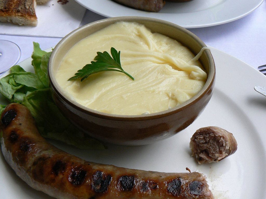 Aligot filant servi en cassolette avec une saucisse grillée et de la salade