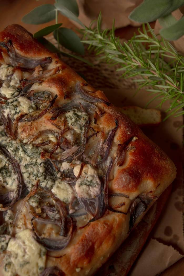 Focaccia maison parsemée de morceaux de Fourme d'Auvergne, oignons rouges caramélisés et romarin
