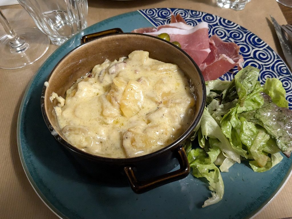 Truffade gratinée servie en cocotte avec du jambon cru et de la salade